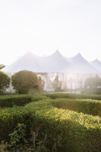Sailcloth tent wedding reception set in a landscaped garden, with soft light filtering through the tent at sunset.