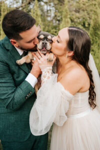 Bride and groom sharing a joyful moment with their dog on their wedding day